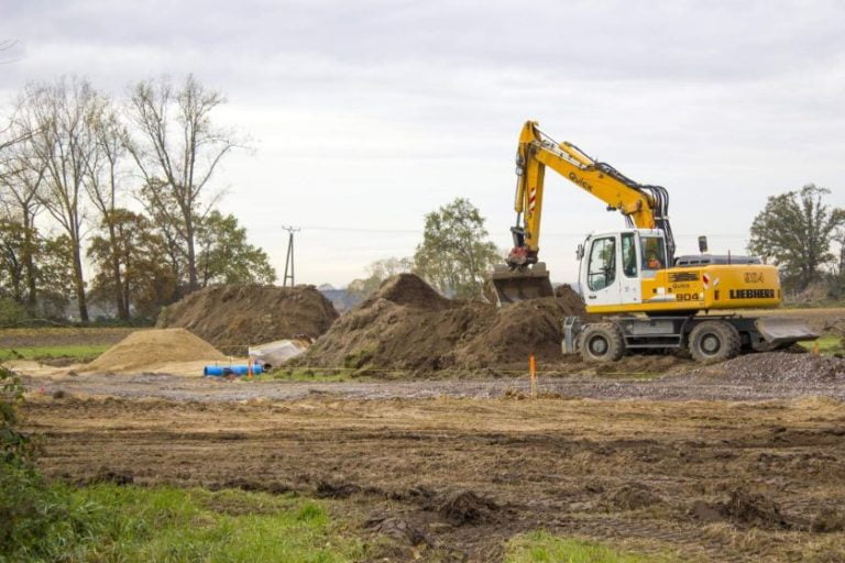 Yellow excavator digging and levelling out soil on a commercial excavation site