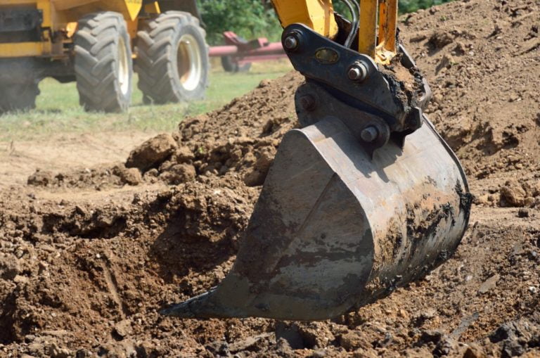 Yellow excavator digging up soil for commercial purposes