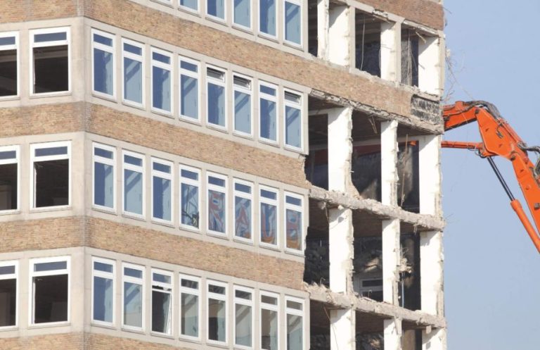 Large commercial building being demolished by a cutter machine