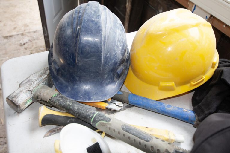 yellow and blue hard hats on a table, used for demolition safety, with several demolition tools underneath