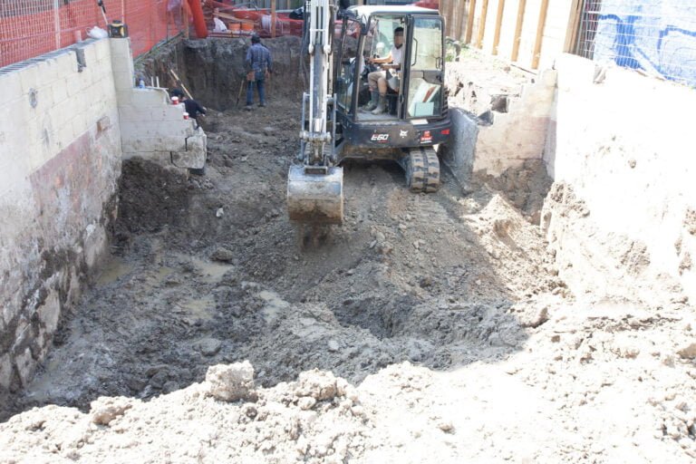 site preparation moving soil with an excavator and workers manually digging to finalize underpinning preparations
