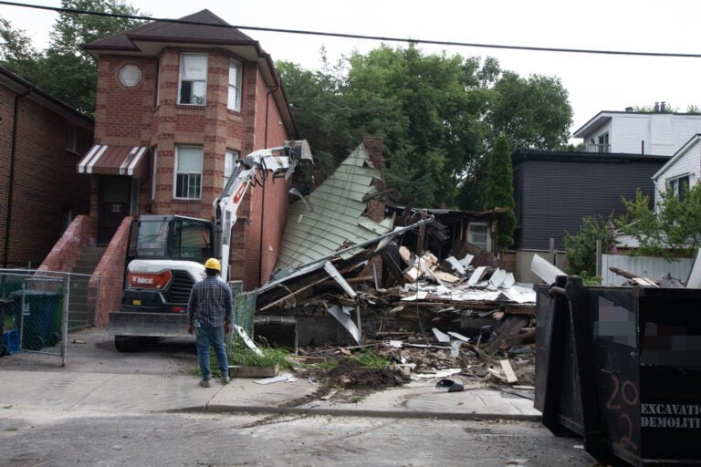 worker watches whilst an excavator takes down the exterior side wall of a house