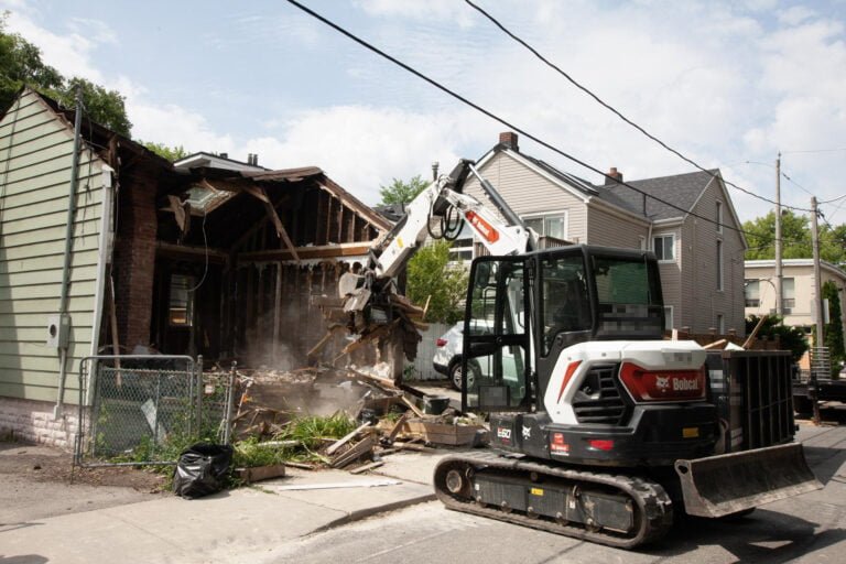 excavator moving debris from an exterior demolition towards the bin